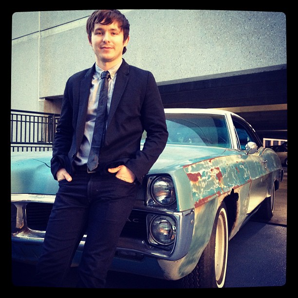 Marshall Allman posing with a blue car from the set of 'Blue like Jazz'